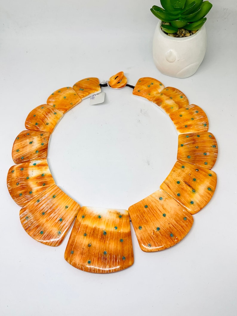 May include: A necklace made of orange and white bone with turquoise accents. The necklace is made of multiple pieces of bone that are shaped like a fan. The bone is polished and has a natural pattern.