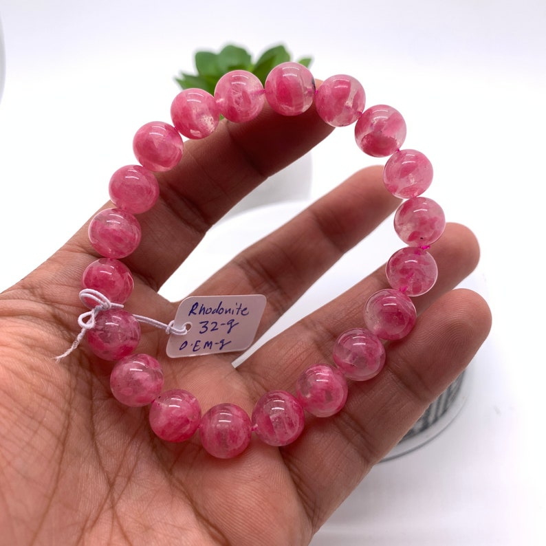 May include: Pink Rhodonite gemstone bracelet with 14 beads. The bracelet has a tag that reads "Rhodonite 32-7 GEM".