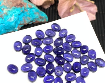 May include: A collection of oval-shaped, deep purple gemstones. The stones are smooth and polished, with a slight sheen.