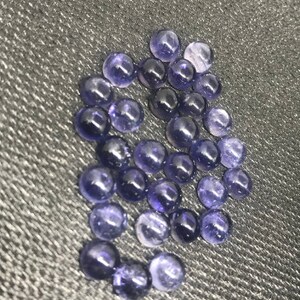 May include: A collection of round, purple gemstones with a smooth, polished finish. The stones are arranged in a loose cluster on a gray textured surface.
