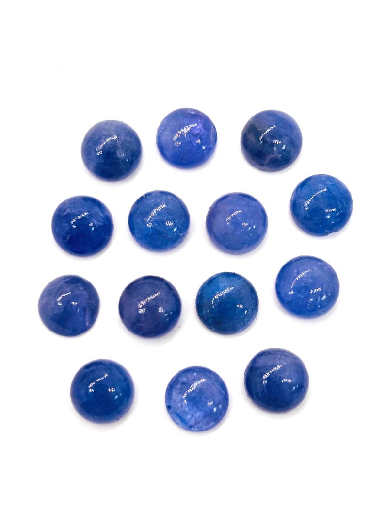 May include: A collection of fourteen round, polished blue gemstones. The stones vary slightly in shade, with some appearing a deeper, richer blue than others. The gemstones are arranged against a plain white background.