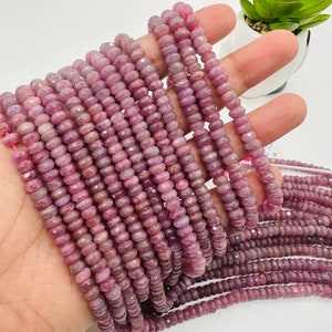 May include: A strand of pink ruby beads, faceted and round, strung on a clear thread. The beads are approximately 4mm in diameter and are arranged in a straight line.