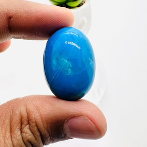May include: A bright blue oval cabochon gemstone with white veins and a smooth, polished surface.
