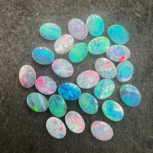 May include: A collection of oval-shaped opal gemstones in various shades of blue, green, and pink. The opals are iridescent and have a shimmering effect.