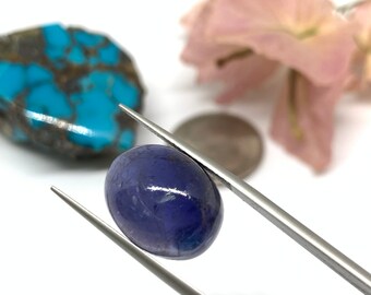 May include: A close-up of a purple oval gemstone held by tweezers. The gemstone is smooth and shiny, with a slight shimmer.