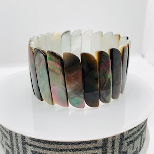 May include: A black and iridescent shell bracelet with a curved design. The bracelet is made of multiple pieces of shell that are joined together.
