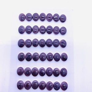 May include: A collection of 42 oval-shaped, polished gemstones in shades of purple and white, arranged on a white card. The gemstones measure 8x10mm. The card also has the text "8x10mm" and "42pcs".