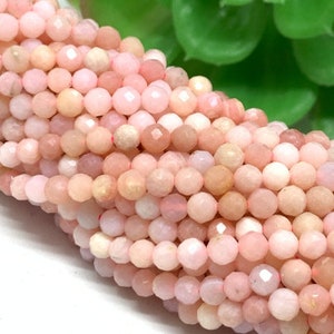 May include: A strand of pink opal beads, each bead is faceted and has a slightly irregular shape. The beads are arranged in a loose pile, showing the variation in color and texture.