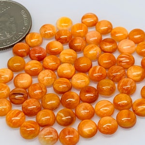 Op de afbeelding: Een verzameling van 30 ronde, oranje en witte, gepolijste edelsteencabochons. De cabochons zijn ongeveer 1,2 cm in diameter.