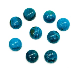 May include: Nine round, polished cabochon gemstones in shades of turquoise and teal are arranged on a white background. The stones have a marbled appearance with swirls of color, and vary slightly in hue.