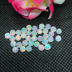 May include: A collection of round, white opal cabochons with iridescent rainbow flashes. The opals are approximately 6mm in diameter and are perfect for jewelry making.