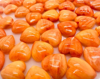 Könnte beinhalten: Eine Sammlung von herzförmigen orangefarbenen und roten Edelstein-Cabochons. Die Cabochons sind poliert und haben eine glatte, glänzende Oberfläche.