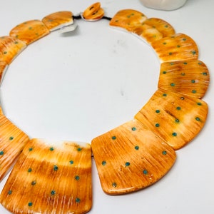 May include: A necklace made of large, rectangular, polished bone beads with a light brown and white marbled pattern. The beads are accented with small, turquoise-colored dots.