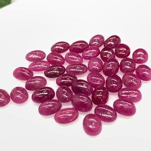 Puede incluir: Una colecci&oacute;n de piedras preciosas de rub&iacute; rosa de forma ovalada. Las piedras son lisas y pulidas, con un ligero brillo.