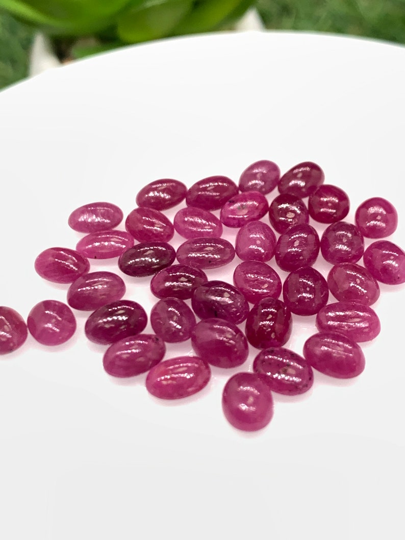 Puede incluir: Una colecci&oacute;n de piedras preciosas de rub&iacute; rosa de forma ovalada. Las piedras son lisas y pulidas, con un ligero brillo.