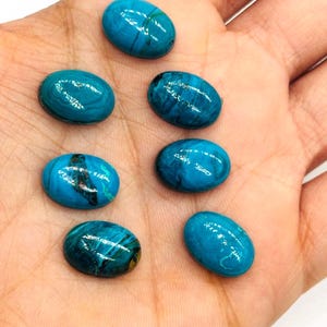 May include: Seven oval-shaped, polished gemstones in varying shades of turquoise and teal. The stones have a glossy finish and exhibit natural veining patterns. The gemstones are displayed on a light-colored surface.