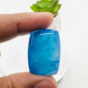 May include: A smooth, light blue cabochon gemstone with white veins. The gemstone is rectangular and has a polished finish.