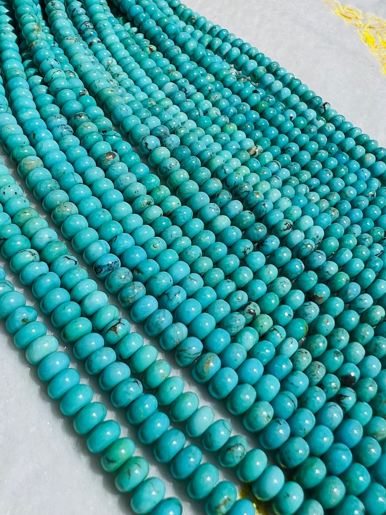 May include: A strand of turquoise beads, each bead is a light blue color with dark blue and brown veins. The beads are round and smooth, and they are arranged in a row.