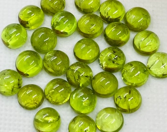 Könnte beinhalten: Eine Sammlung von 20 runden, grünen Peridot-Edelsteinen. Die Steine sind glatt und poliert und haben einen leichten Schimmer.