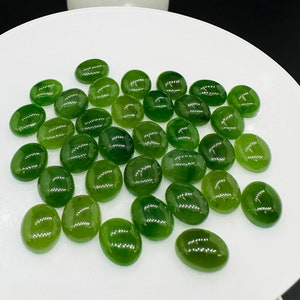 May include: A collection of smooth, oval-shaped green jade stones on a white plate. The stones are various shades of green, from light to dark.