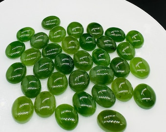 May include: A collection of smooth, oval-shaped green jade stones on a white plate. The stones are various shades of green, from light to dark.