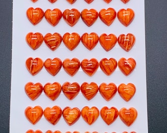 May include: A collection of 42 heart-shaped beads, each 10mm in size, arranged on a white surface. The beads are a warm orange color with a wood-grain pattern. The image is taken from a top-down perspective.