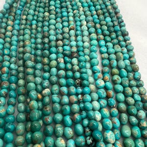 May include: Strands of turquoise-colored beads. The beads are a mix of round and oval shapes, with variations in color from light teal to deep sea green. Some beads have brown and tan markings, adding to their natural appearance. The beads are strung together, ready for jewelry making.