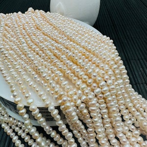 May include: A strand of white freshwater pearls, with a slightly off-white hue, arranged in a pile. The pearls are small and round, with a smooth, polished surface.