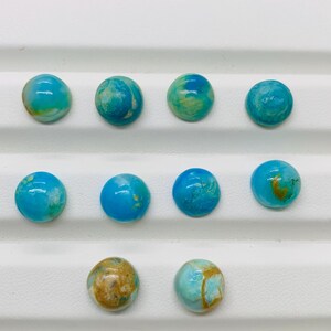May include: Ten round turquoise cabochons with brown and white marbling. The cabochons are arranged in three rows on a white surface.