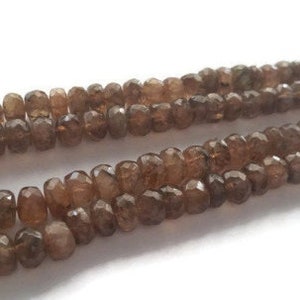 May include: A strand of brown gemstone beads. The beads are faceted and have a slightly irregular shape. The beads are strung on a clear thread.