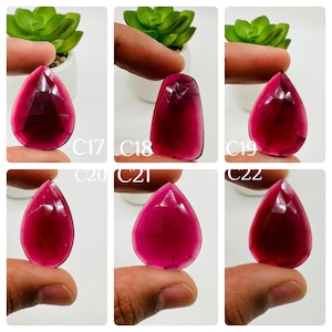May include: Six close-up images of a deep red gemstone, cut in a teardrop shape. The gemstone is held in a hand, with the background blurred.