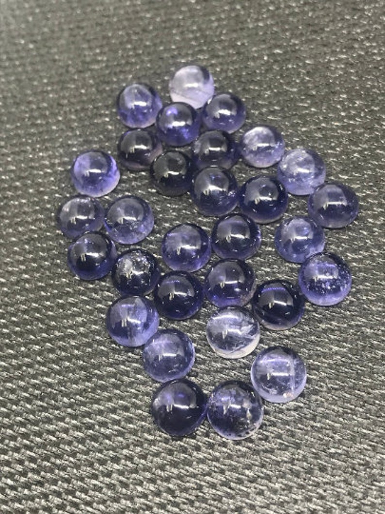May include: A collection of round, purple gemstones. The gemstones are smooth and polished, with a slight shimmer.