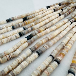 May include: A strand of white, gray, and black shell beads. The beads are small and round, and they are strung together on a thin cord. The beads are arranged in a random pattern, and they are all different sizes and shapes.