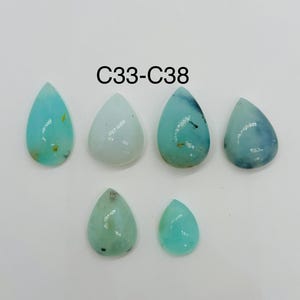 May include: Six teardrop-shaped gemstones in shades of blue and green are arranged on a white surface. The gemstones vary in color, from light blue to a deeper teal, with some showing darker inclusions. The text "C33-C38" is displayed above the gemstones.