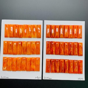 Może przedstawiać: Dwa zestawy pomarańczowych prostokątnych elementów, każdy ułożony na białej karcie. Elementy mają wymiary 8x24mm, a na karcie znajduje się 24 sztuki. Elementy mają błyszczące wykończenie i wygląd słojów drewna.