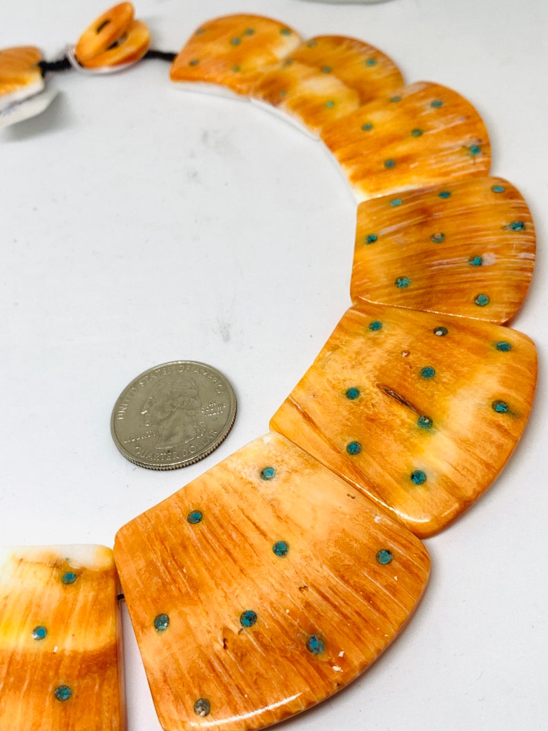 May include: A necklace made of bone with turquoise accents. The bone is a light brown color and has a natural wood grain pattern. The turquoise accents are small and round, and they are evenly spaced throughout the necklace.