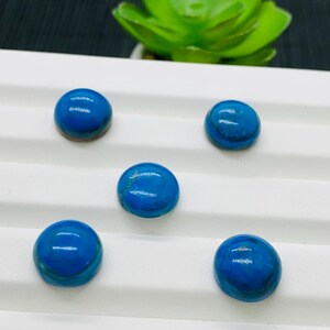 May include: Five round, blue cabochon gemstones with a white background.