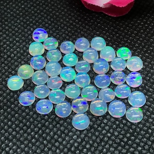 May include: A collection of round, iridescent opal cabochons in various shades of white and blue. The opals are smooth and polished, with a slight shimmer.
