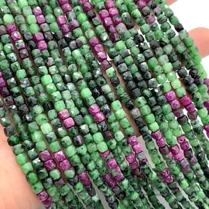 Może przedstawiać: Szereg zielonych i różowych koralików z kamieni szlachetnych. Koraliki są fasetowane i mają kwadratowy kształt. Koraliki są nawleczone na przezroczystą nić.