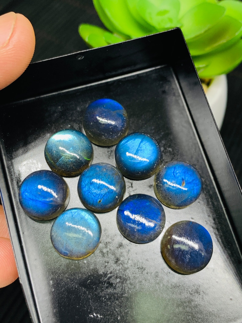 May include: A collection of ten round, iridescent blue labradorite gemstones in a black tray. The gemstones have a variety of shades of blue and gray.