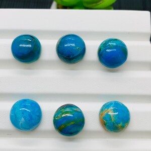 May include: Six round, blue and green cabochon stones with a marbled pattern. The stones are arranged in two rows of three on a white surface.