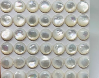 May include: A sheet of white paper with 49 round, white mother-of-pearl cabochons. The cabochons are arranged in 7 rows of 7. The paper has the text "10mm" and "Ebony" written on it.