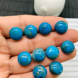 May include: A collection of ten round, blue and green cabochon gemstones with gold flecks. The gemstones are smooth and polished.
