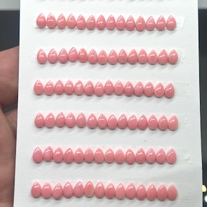 May include: A white card featuring 98 light pink, teardrop-shaped cabochons arranged in seven horizontal rows. Each cabochon has a smooth, glossy finish. The bottom left corner displays the text 4x6mm and the bottom right shows 98pcs.