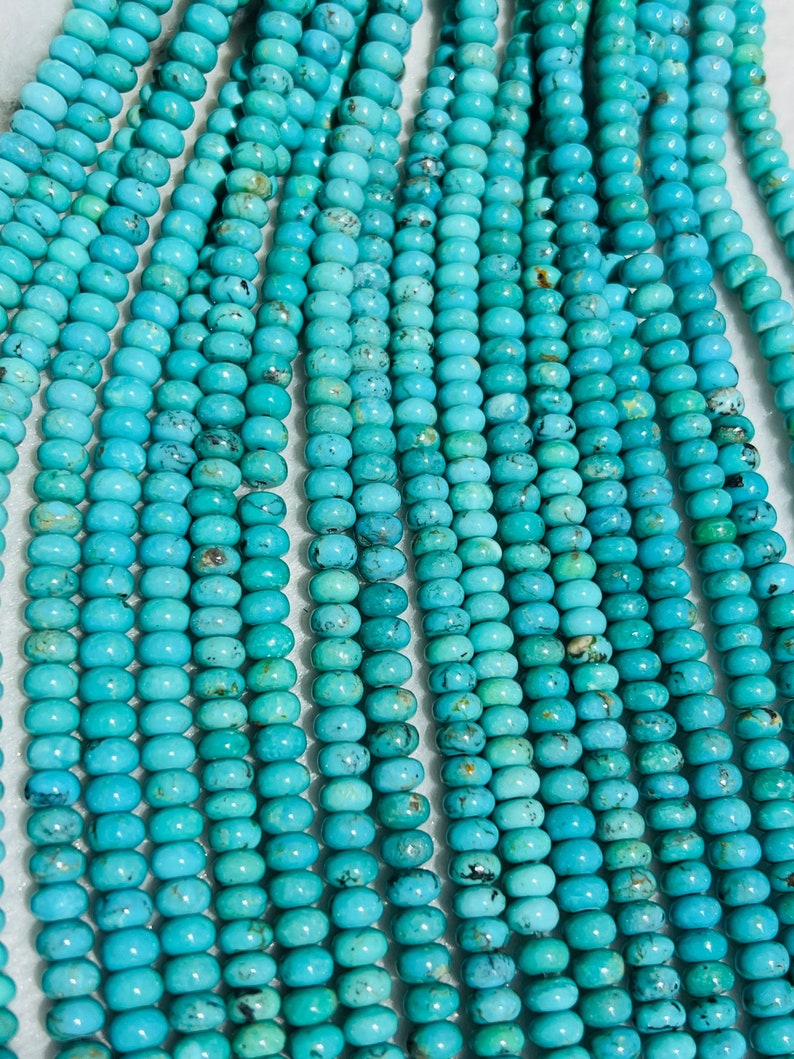 May include: A strand of turquoise beads, each bead is a light blue color with dark brown and black marbling. The beads are round and smooth.