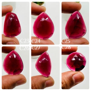 May include: Six faceted, teardrop-shaped, deep red gemstones. The gemstones are held in the hand, with the tips of the teardrops pointing upwards.