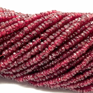 Può includere: Un filo di perline di pietra preziosa sfaccettata rosso scuro. Le perline sono piccole e hanno una forma leggermente irregolare.