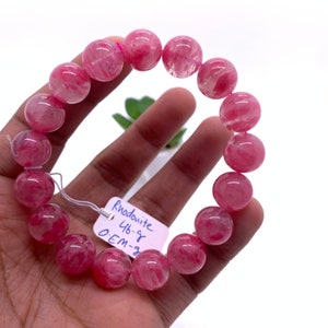 May include: Pink Rhodonite gemstone bracelet with 10 round beads. The bracelet is 6.5 inches in circumference and has a tag that reads "Rhodonite 46-8 OEM-3".
