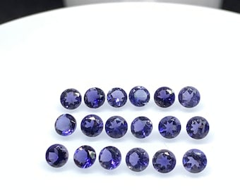 May include: A collection of 16 round, faceted, purple gemstones. The gemstones are arranged in rows on a white surface.