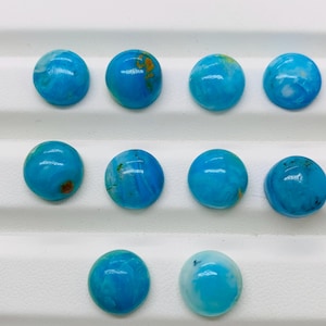 May include: Ten round, blue cabochon gemstones with white and gold marbling. The stones are arranged in three rows on a white surface.